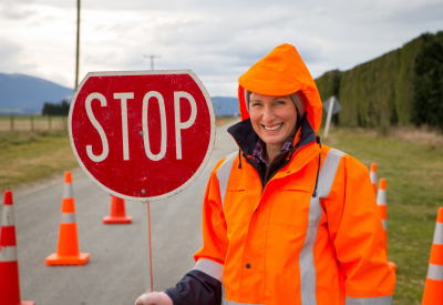 Eine Frau aus einem Strassenteam bedient ein Stoppschild an einer Gefahrenstelle auf einer Landstraße in Canterbury, Neuseeland