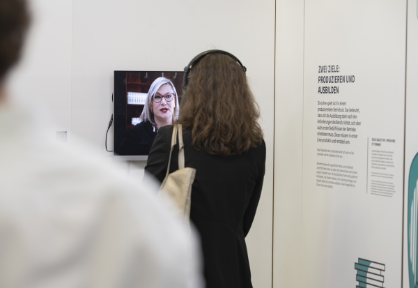 Frau mit Kopfhörer steht vor einem Screen der Ausstellung «Im Herzen der Berufslehre» 