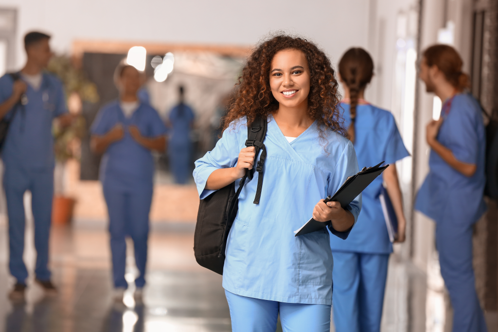 Junge Frau in Medizinal-Arbeitskleidung steht in Korridor und blickt in Kamera