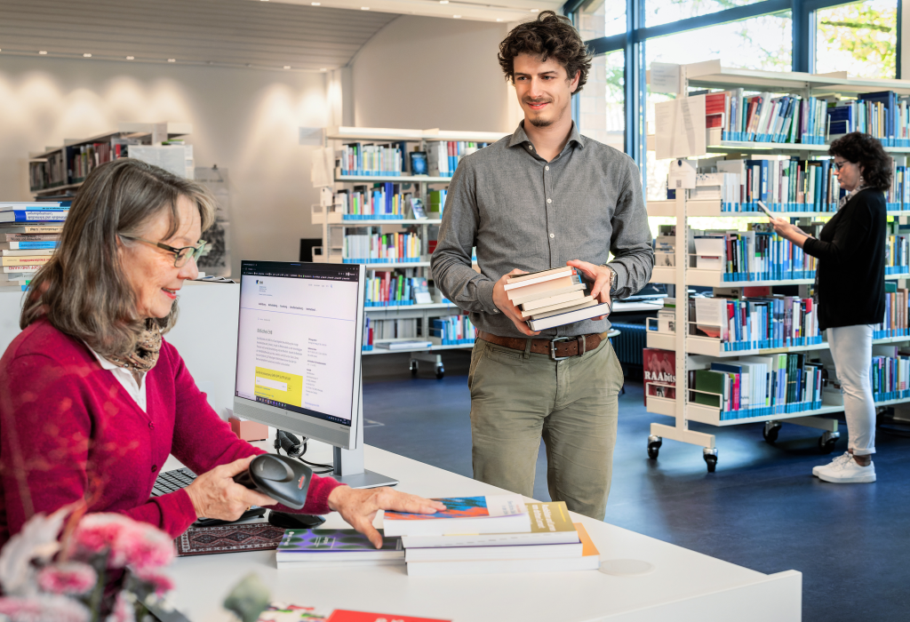 Ein Mann leiht bei einer Frau am Empfang der Bibliothek Bücher aus