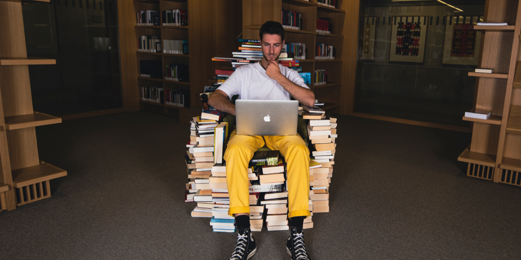 Person sitzt in der Bibliothek auf einem Stuhl aus Büchern