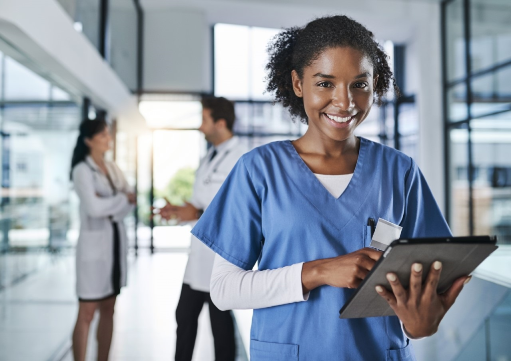 Unsere Patientenakten sind alle digitalisiert. Aufnahme einer jungen Ärztin, die in einem Krankenhaus ein digitales Tablet benutzt, mit ihren Kollegen im Hintergrund.